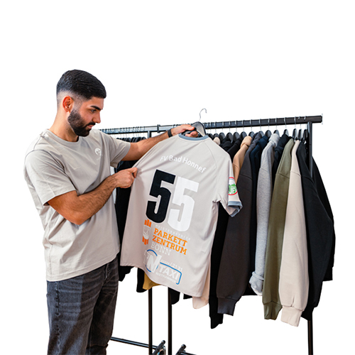ein Mann hält ein Hemd mit einer Nummer in der Hand Rheinpiraten Agentur in Rheinbreitbach, Bonn und Köln– Grafikdesign, Webdesign, Werbetechnik & Textilveredelung